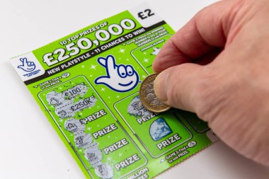 Londra mı? UK- 09.27.2023. Kartı çizmek için bozuk para kullanan bir oyuncuyla beyazdan izole edilmiş Ulusal Loto kazı-kazan kartları..