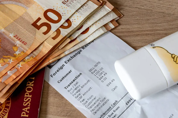 A travel money, holiday and money exchange concept with Euro bank notes, a passport, sun cream on top of a currency exchange receipt.