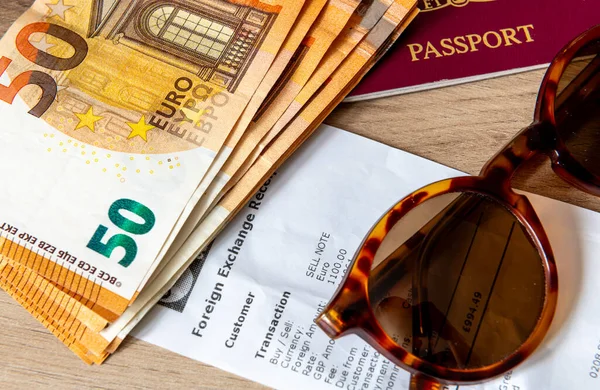 A travel money, holiday and money exchange concept with Euro bank notes, a passport and sunglasses on top of a currency exchange receipt.