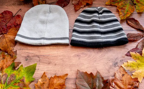 Woolly hats, wool hats with a circle of fallen leaves on a wooden background.