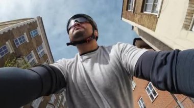Tam teçhizatlı, kask takan ve gözlüklü bir bisikletçinin şehir caddesinde iki tarafında da yüksek binaları olan bir bisiklet sürüşü..