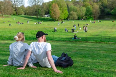 Londra mı? UK- 04.14.2023. Kalabalık, güneşli bir bahar gününde parkın yeşil çim tarlasında dinleniyor ve eğleniyor..