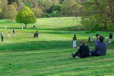 Londra mı? UK- 04.14.2023. Kalabalık, güneşli bir bahar gününde parkın yeşil çim tarlasında dinleniyor ve eğleniyor..