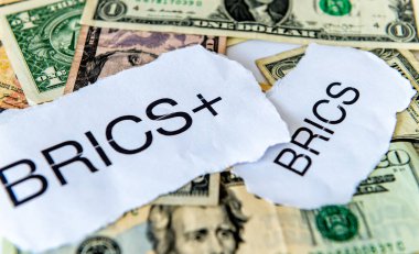 A dedollarisation concept with the words BRICS and BRICS+ on top of a loose pile of US dollar bills. clipart