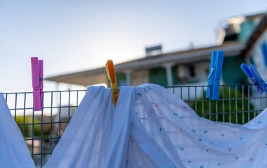 Çamaşırlar dışarıda, renkli mandallarla tutulan tel bir çitin üzerinde kurutuluyor..