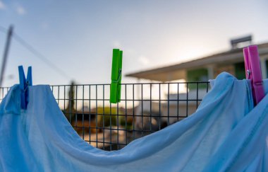 Çamaşırlar dışarıda, renkli mandallarla tutulan tel bir çitin üzerinde kurutuluyor..