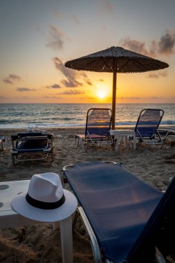 Güneşli yataklı ve şemsiyeli bir plajda gün batımı.