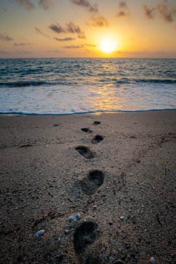 Kumsalda ayak izleri gün batımında denizde kayboluyor..