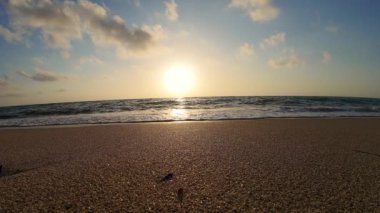 Yavaş çekim günbatımı görüntüsü kumlu bir plaja vuran dalgalar..
