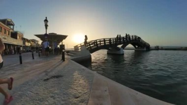 Lefkada Town, Lefkada, Yunanistan-06.30. 2024. Başkentin gezinti alanının zaman aşımı ve turistlerin güzel günbatımında selfie çektiği ünlü tahta köprü..