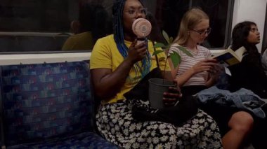 Londra mı? Birleşik Krallık-08.15.2024. Sıcak bir yaz gününde serinlemek için elektrikli yelpaze kullanan Londra metro vagonunda bir yolcu..