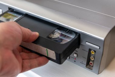 Antika bir video oynatıcıya video kaset yerleştiren bir kişi.