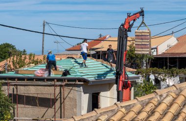 Lefkada, Yunanistan... 10.08.2024. Bir vinç seramik çatı kiremiti taşıyor. Tadilat yapılan bir binanın çatısında çalışıyor..