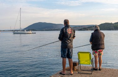 Lefkada, Yunanistan... 10.18.2024. Amatör balıkçılar, sakin bir denizde, güzel bir sabahta rıhtımda balık tutuyorlar..