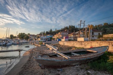 Lefkada, Yunanistan... 10.18.2024. Lygia köyünün liman sahilinde, sabah ışığında güzel gökyüzü bulutlarıyla eski, ahşap bir tekne..