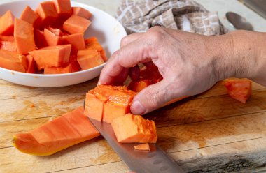 A person preparing a ripe papaya for eating using a knife to remove the flesh from the skin. clipart