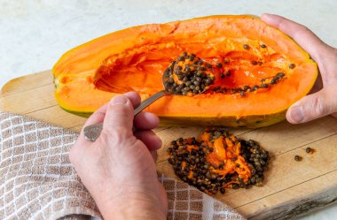 Büyük olgun bir papayanın siyah tohumlarını kaşıkla kepçeleyen bir insan..