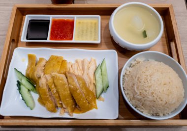 Üç çeşit sos ve bir kase çorba ile servis edilen bir tepside sunulan Hainanese tavuğu pilavı..