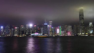 Hong Kong. Çin... 02.20.2025. Tsim Sha Tsui 'den, ikonik gökdelenlerin ve işlek su yollarının ışık gösterisiyle Orta Bölge' ye bir gece geçişi..