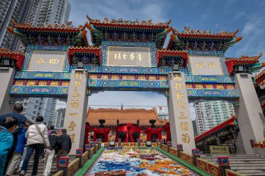 Hong Kong. Çin... 02.24.2025. Shik Sik Yuen Wong Tai Sin Tapınağı 'nın süslü kapısı. Ziyaretçiler ana tapınak kompleksine girmek için merdivenleri çıkıyorlar..