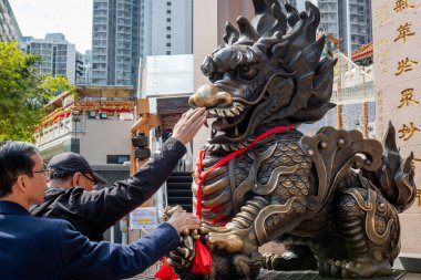 Hong Kong. Çin... 02.24.2025. Shik Shik Sik Yuen Wong Tai Sin Tapınağının girişinde bir bronz ejderha heykeli. Ziyaretçisi ona iyi şans ve şans getirmesi için dokunuyor..
