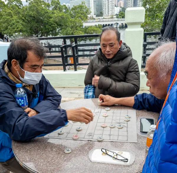 Hong Kong. Çin - 02.23.2025. Sha Tin Park 'ta Çin satrancı oynayan iki yaşlı adamın etrafı izleyicilerle çevrili..