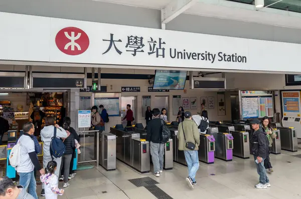Hong Kong. Çin - 02.23.2025. Girişin üstünde logo ve isim işareti olan MTR Üniversite İstasyonu ve bilet engellerini kullanan yolcular..