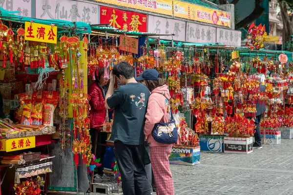 Hong Kong. Çin... 02.24.2025. Wong Tai Sin Tapınağına gelen ziyaretçiler tapınak meydanındaki dini dükkanlardan alışveriş yapıyorlar..