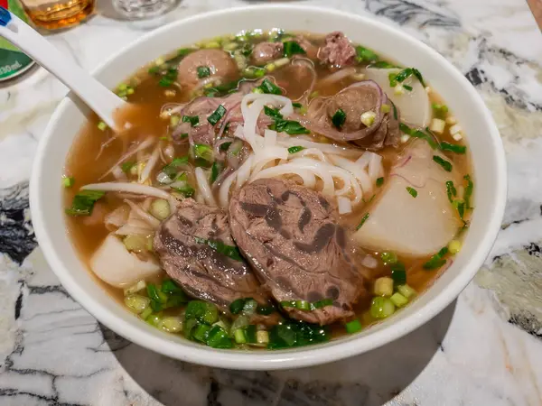 Bir kase Ho Fun Noodles Çorbası et dilimleri, köfteler ve mooli, dilimlenmiş soğan ve doğranmış taze soğanla süslenmiş..