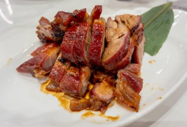 Koyu soya soslu bir tabakta servis edilen Çin usulü barbekü rostosu..