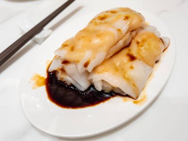 Har cheung fun ya da karidesli pilavlı şehriye dürümü oval bir tabakta servis edilen lezzetli, koyu bir sosla servis edilen mermer arka planda izole edilmiş..