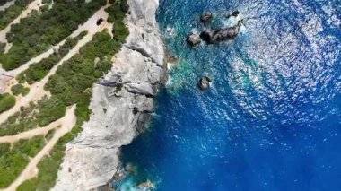 Derin mavi denizde engebeli bir sahil ve güneş ışığının parlaklığını gösteren bir Yunan adasının göz kamaştırıcı manzarası..