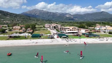 Lefkada, Yunanistan... 05.19.2025. Vassiliki Sahili 'nin yan görüntülerinde tatil daireleri, sahil tesisleri ve su sporlarından hoşlanan turistler görülüyor..