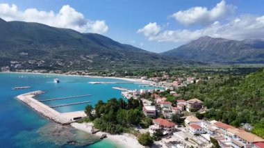 Turistlere su sporları sağlayan tekne limanı ve uzun plajlı bir Yunan adası yerleşiminin hava görüntüleri.