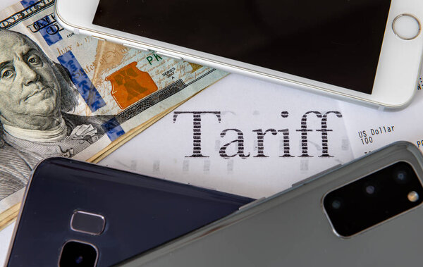 Пачка купюр в долларах США и различные мобильные телефоны на печатном слове тариф. Стоимость жизни, концепция тарифной инфляции.