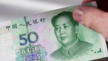 Beyaz arka planda Çin Yuan banknotlarını sayan birinin yakın plan görüntüsü..