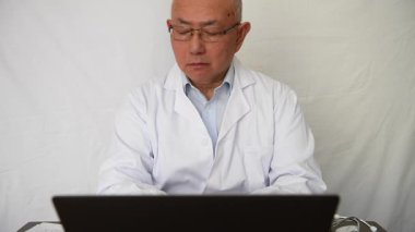 A doctor or laboratory researcher reading reports on a desk and working on a laptop computer.