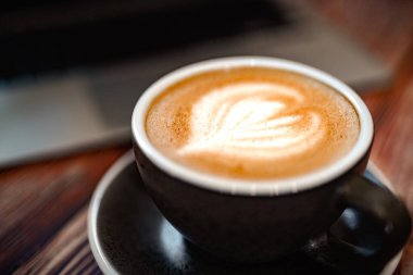 Tahta masadaki dizüstü bilgisayarlı sıcak soya sütlü kahvenin üst görüntüsü. rahat çalışma masası konsepti.