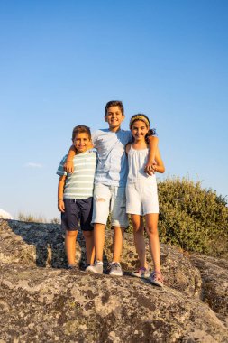 Yaz tatilinde kayanın tepesinde üç çocuk.