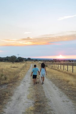 Gün batımında kırsalda el ele yürüyen iki çocuk.