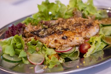Tabakta servis edilen sebzeli ve domatesli ızgara balık salatası.