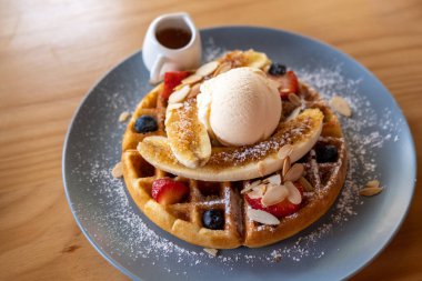 Dondurma ve yabanmersinli waffle, çilek, muz ve bal tabakta servis edilir.