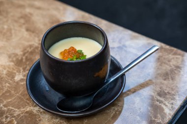 Somon yumurtası ile buğulanmış yumurta, siyah bir kasede servis edilir.