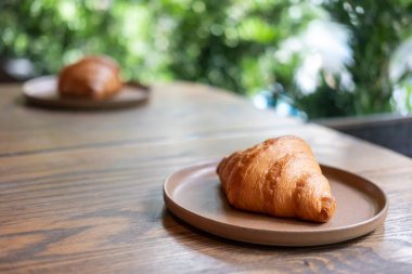 Tabakta servis edilen kruvasan, yeşil bitkinin bulanık arka planıyla masada..