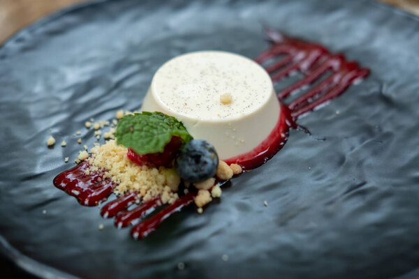 Панна Котта подается на тарелке с ягодами и соусом