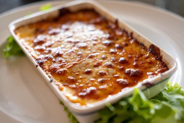 Lazanya kasede servis ediliyor, tabakta sebze var.