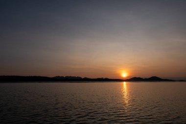 Renkli gökyüzü ve deniz ile gün doğumu manzarası, arka planda ormanın silueti