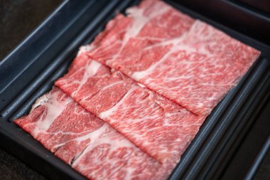 Yakın plan kesilmiş çiğ et, bir tabakta, sıcak bir tencerede pişirilmeye hazır.