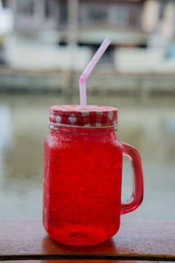 Nehir manzaralı ahşap masada kırmızı içecek suyu.