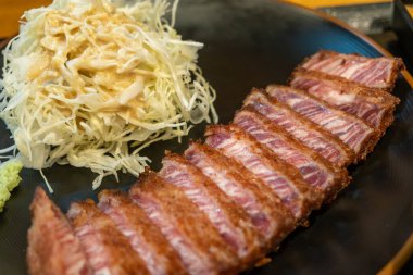 Lahanayla servis edilen Gyukatsu ya da sığır pirzolası. Kızarmış sığır pirzolasından oluşan geleneksel bir Japon yemeği. Taş ızgaranın üstünde.